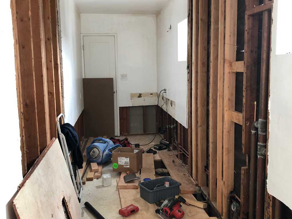 a2mContractors removes the old bathroom wall showing the studs, water pipes and electrical