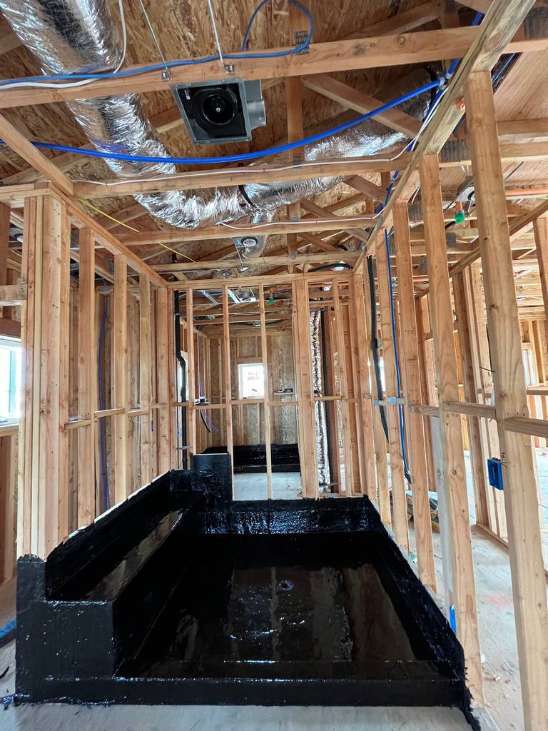 Framed bathroom with new shower base coated in black waterproofing and visible ceiling ductwork.