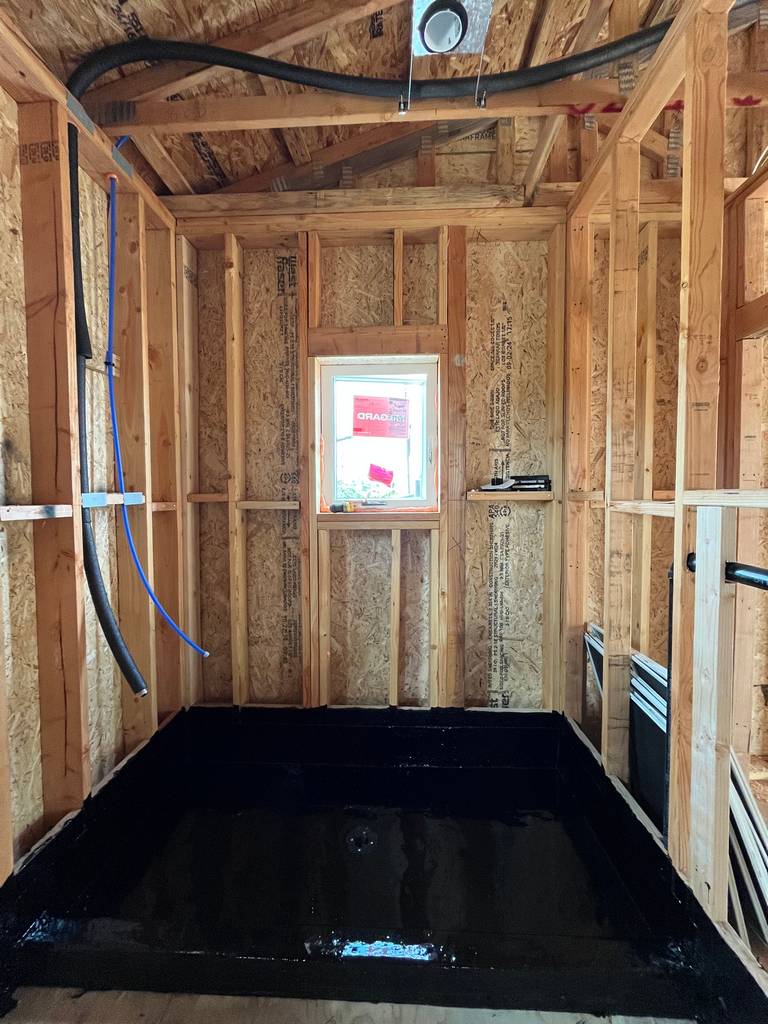 Shower framing and plumbing rough-in with black waterproofed base and exposed studs.