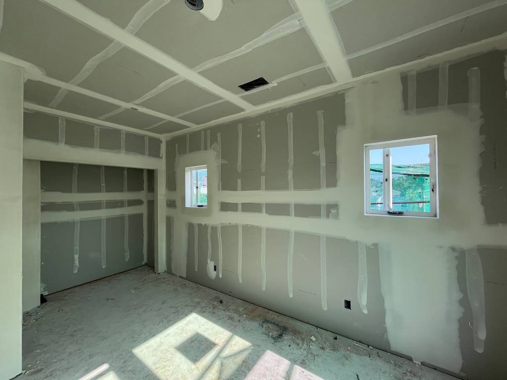 Drywall installation and finishing in corner room with two small windows..
