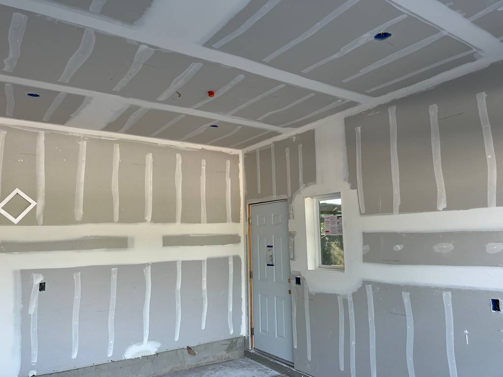 Drywall installed and finished on garage walls with ceiling joints taped.