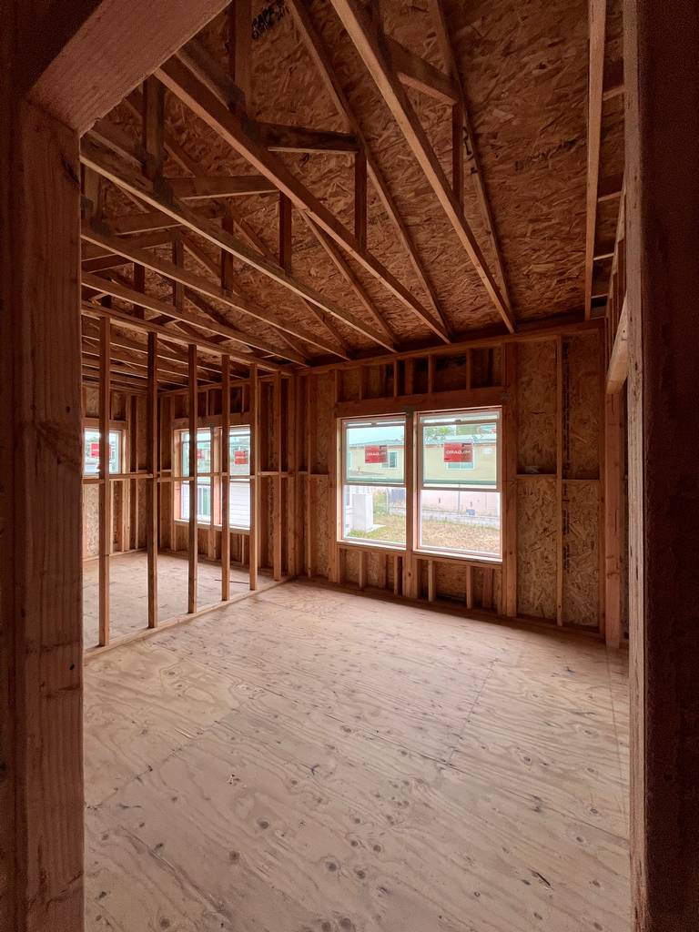 Second-floor interior with angled truss roof framing and large double window overlooking property line.