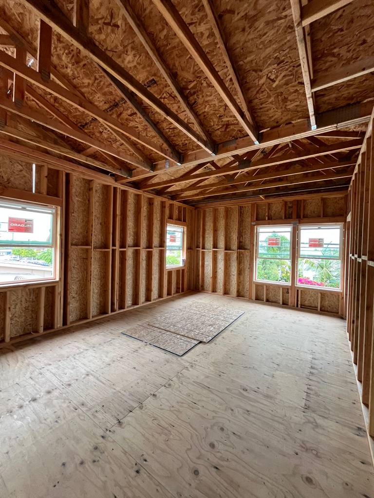 Vaulted ceiling framing with symmetrical window layout and cutout plywood section on floor.
