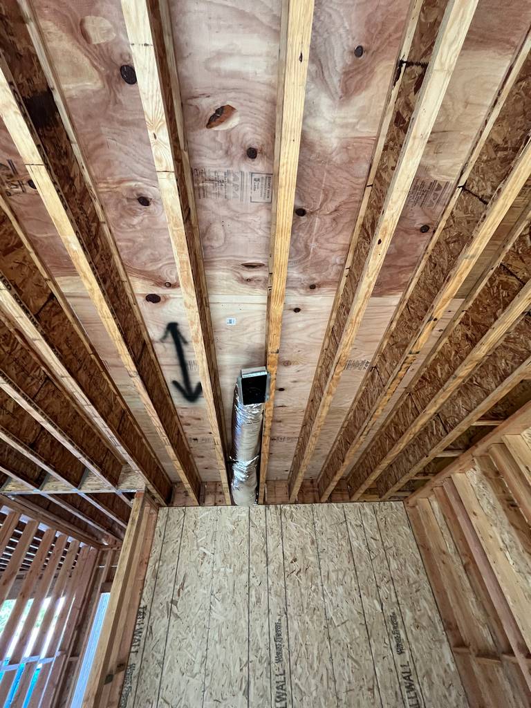 Interior ceiling view with plywood subflooring above and metal HVAC duct running between joists.