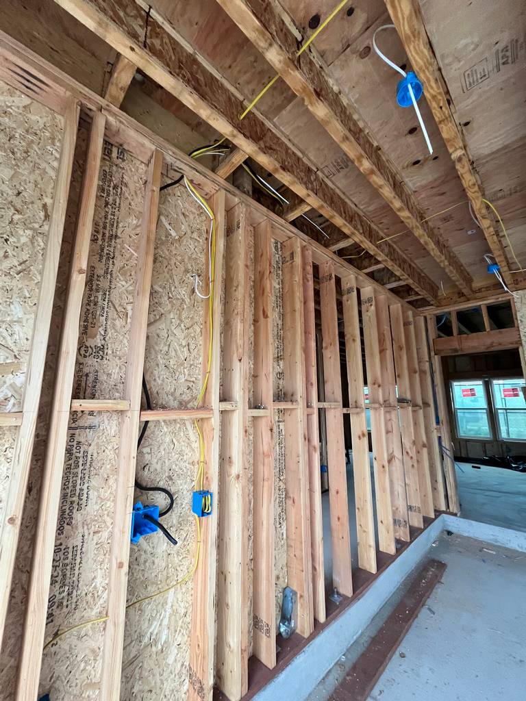 Interior framing with vertical studs and electrical conduit installed. OSB sheathing and rough wiring are visible along the wall.