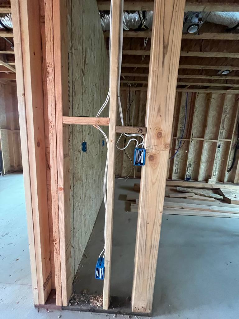 Wall framing with stacked outlet boxes and vertical wiring. New construction showing clean conduit routing and exposed studs.