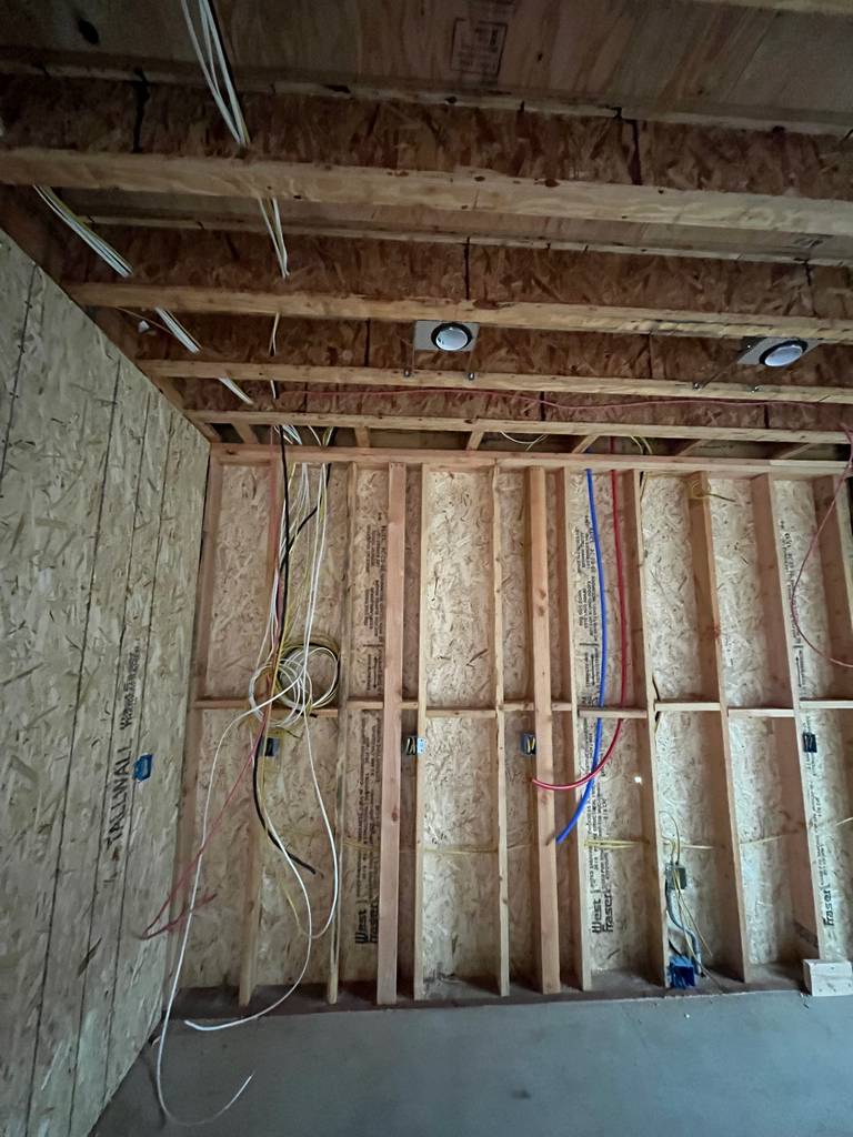 Framing wall packed with electrical wires, conduit, and recessed light boxes. Rough layout prep for utilities is underway.