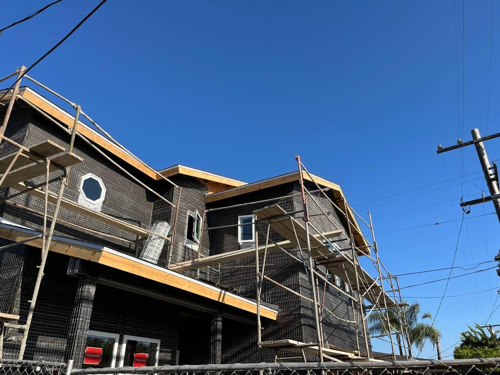 Stucco lath and scaffolding are installed on the upper walls of a two-story residential build during early exterior prep.
