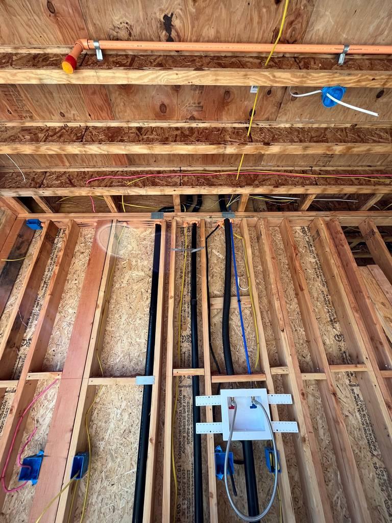 Laundry plumbing and electrical lines installed between wall studs with copper and PEX overhead.