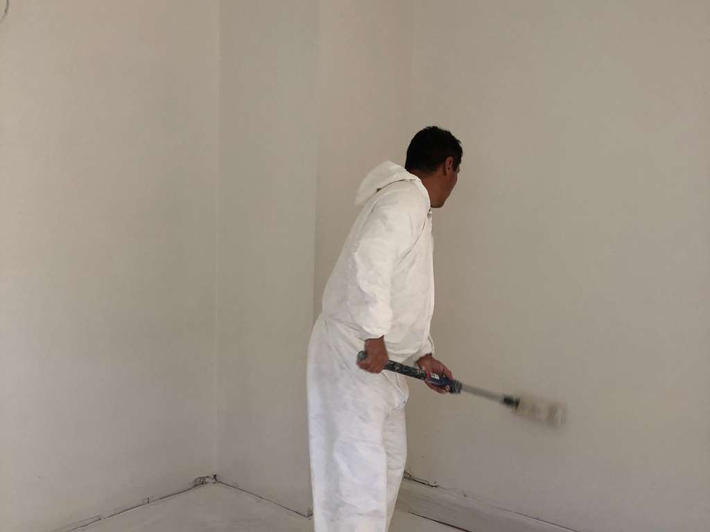 Painter using a paint roller to coat the walls on front room remodel