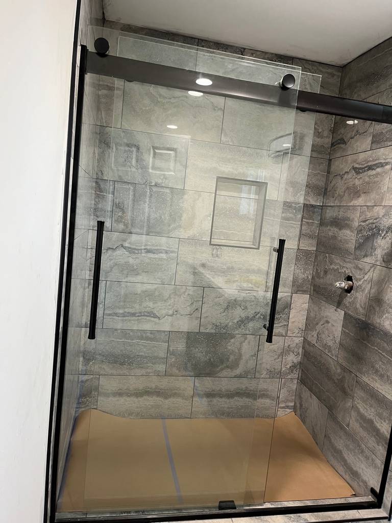 beautiful designed walk in shower with long horizontal marble texture tile  and sliding glass doors with bronze frame.
