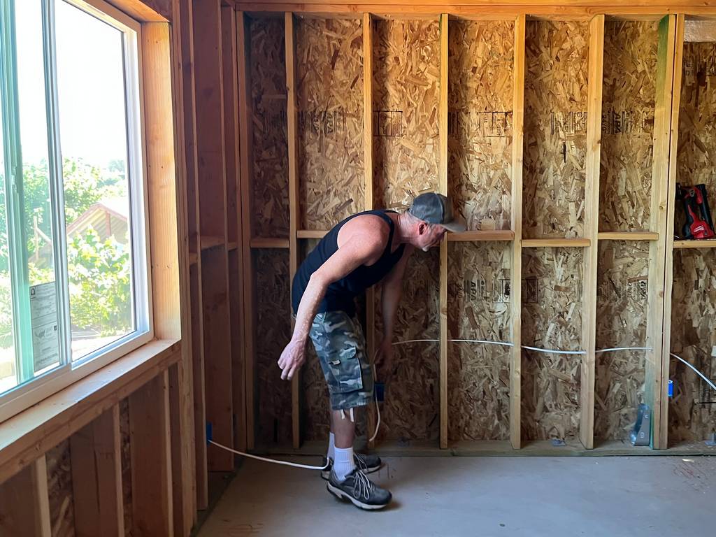 professional electrician pulling romex wiring through open wall studs